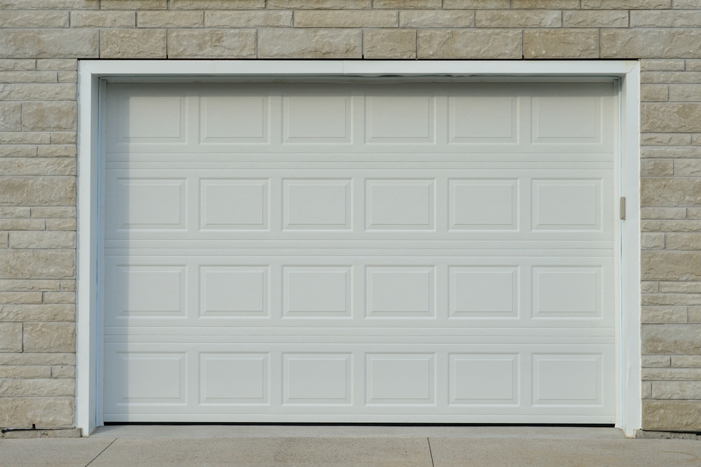 White garage door with a rectangular panel design set in a stone exterior wall.