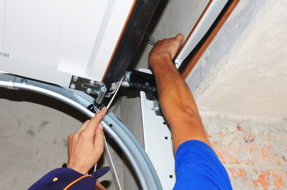 Person installing or adjusting the cable mechanism and hardware on a garage door track, seen from above at close range.
