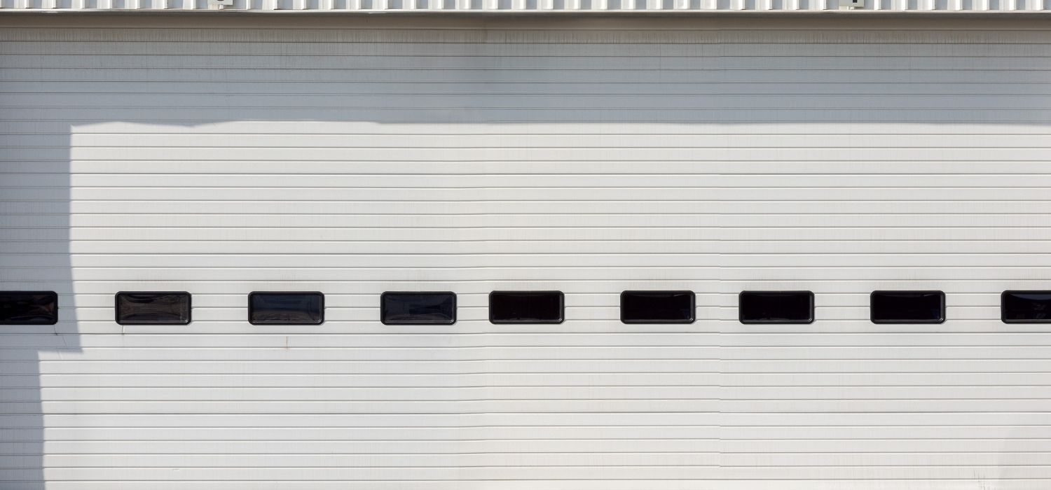 A white industrial garage door with horizontal panels and a row of small rectangular windows near the center, perfect for businesses seeking commercial garage doors in Fayetteville NC.